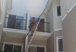 A gutter specialist climbs a ladder to install gutters on an apartment complex in Woodinville, WA