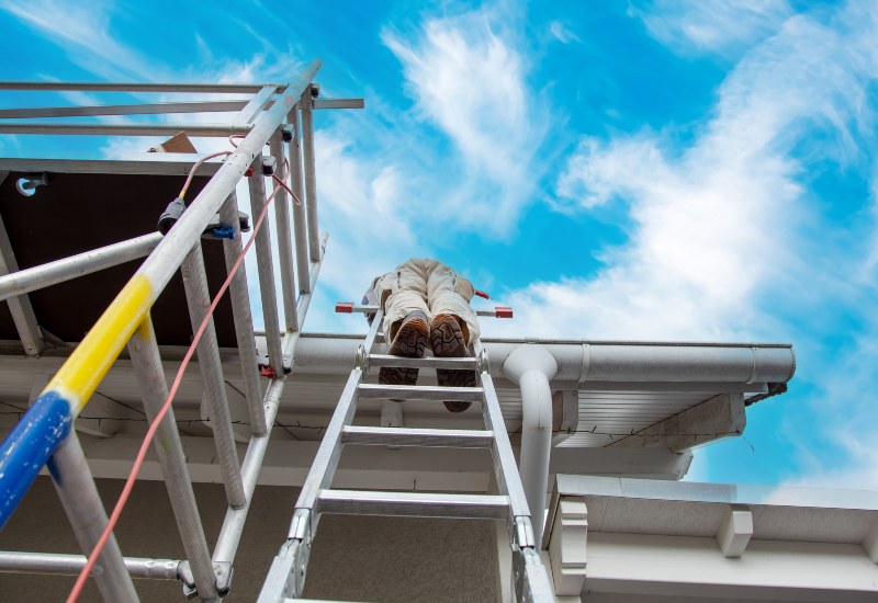 A gutter specialist stands on a ladder fixing a gutter on an apartment building in Kirkland, Washington